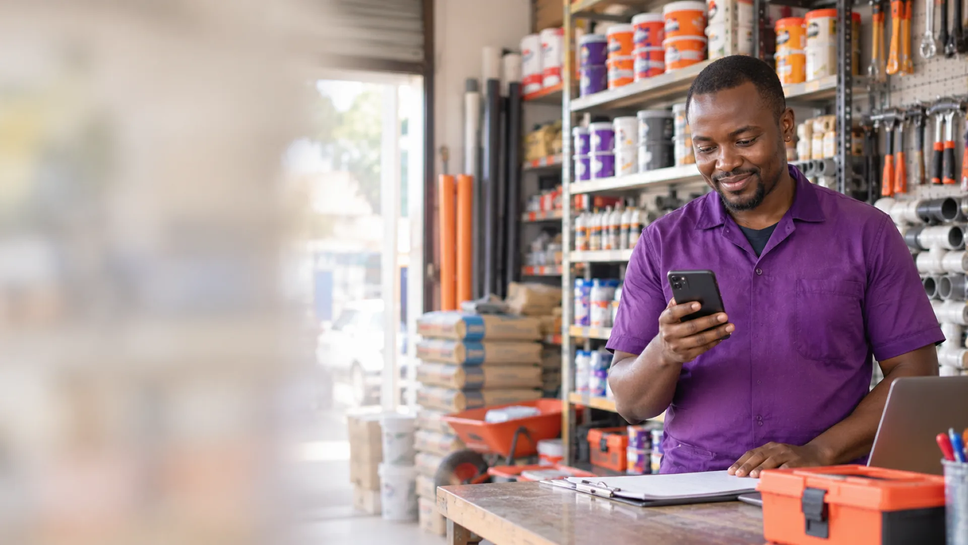 A shop owner checks an order on a phone at the counter of a hardware store